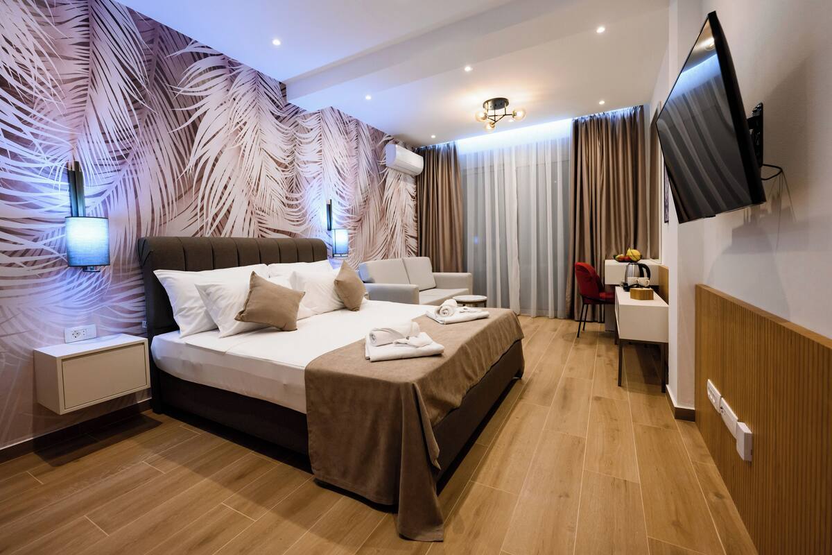 A modern hotel room with a large bed, a desk, a flat-screen TV, and a wall-mounted air conditioner.