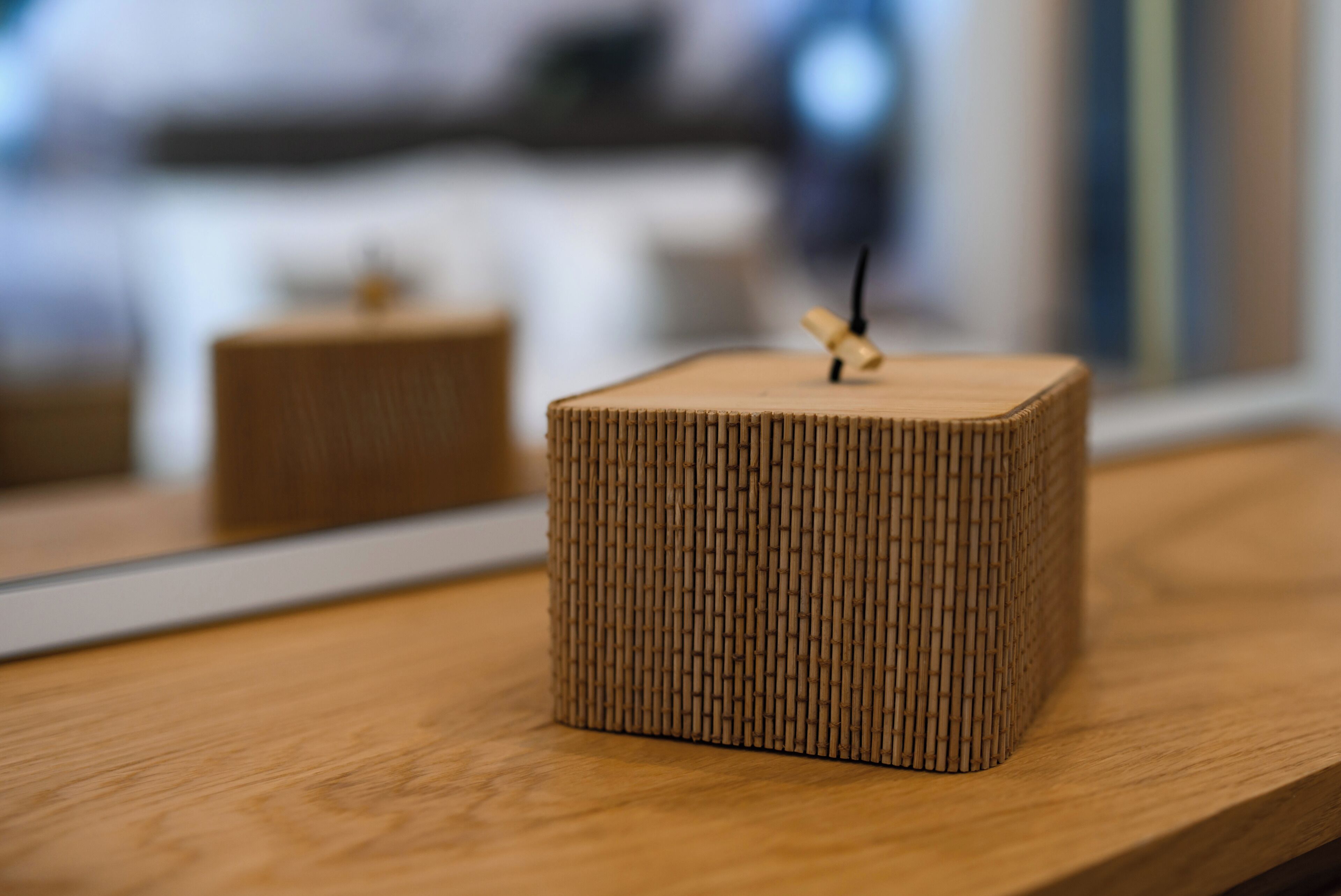 A square, textured wooden object on a wooden surface, possibly a decorative item or a piece of furniture.