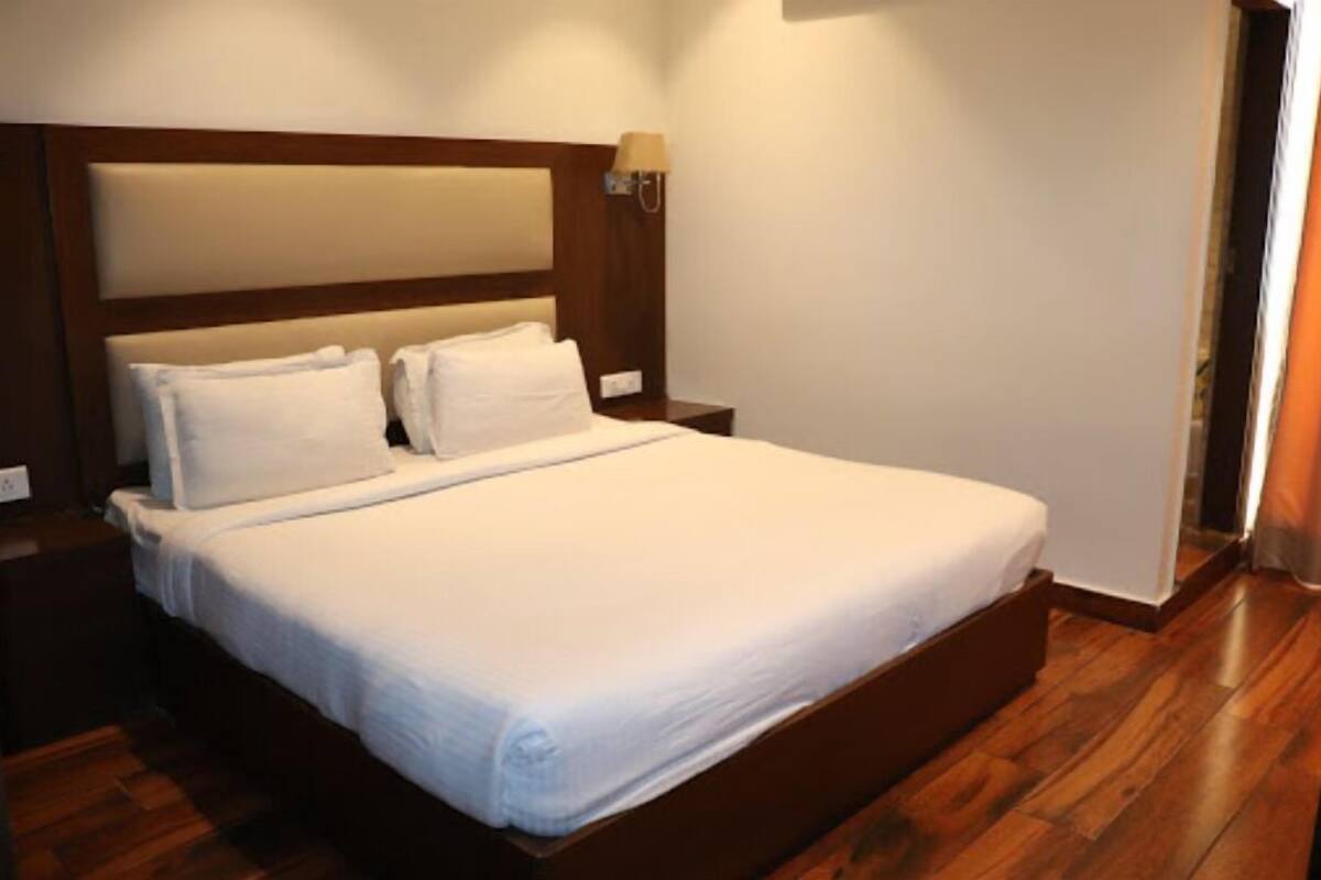 Una cama bien hecha con ropa de cama blanca en una habitación de hotel con suelo y cabecera de madera.