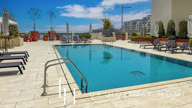 A rooftop pool area with lounge chairs, potted plants, and a clear view of the city skyline.
