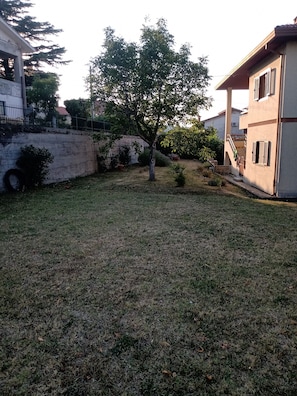 A residential area with a grassy yard, a tree, and a building with a balcony. - Holiday Home "Mare e Lavanda" with Sea View, Private Garden & Wi-Fi (Muggia)