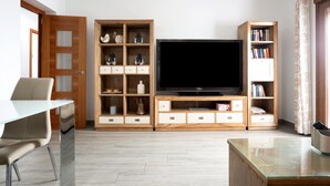 A living room with a TV, wooden shelving, a glass coffee table, and a door.