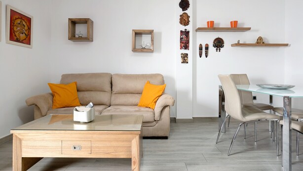 A modern living room with a beige sofa, a glass coffee table, and a dining area with a glass table and chairs.