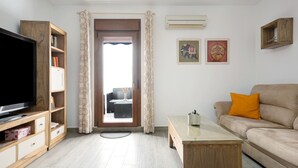 A living room with a television, wooden furniture, a sofa, a coffee table, and a door leading to an outdoor area.