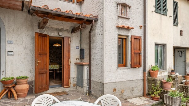Une cour avec une table et des chaises, des plantes en pot et l’entrée d’un bâtiment dotée de volets en bois.