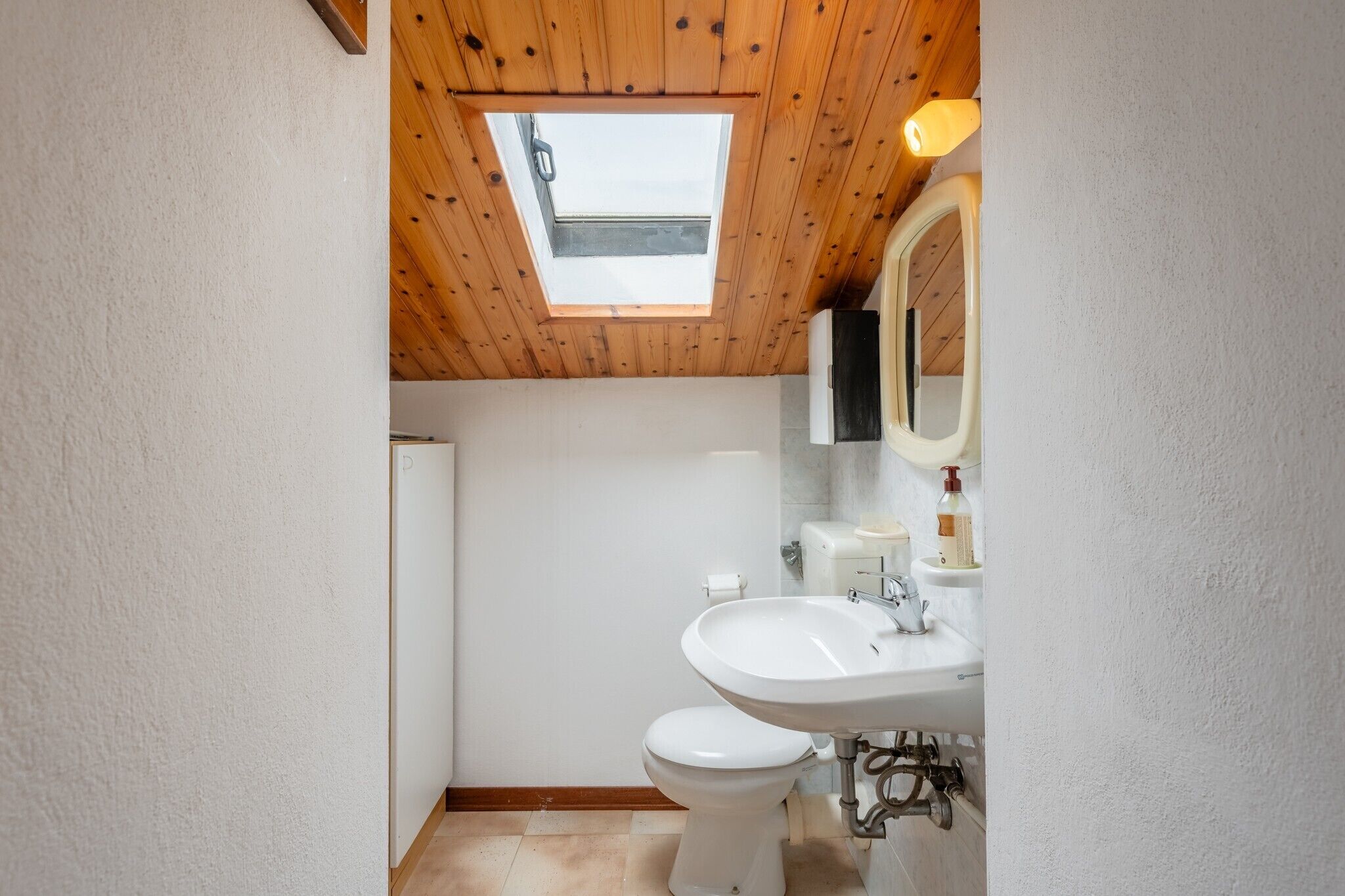 Un bagno con lucernario, WC bianco, lavandino e specchio.