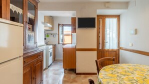Une cuisine compacte dotée de meubles en bois, d’un réfrigérateur, d’un four à micro-ondes et d’un téléviseur fixé au mur.