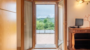 An open door leading to a balcony with a view of greenery and a building.