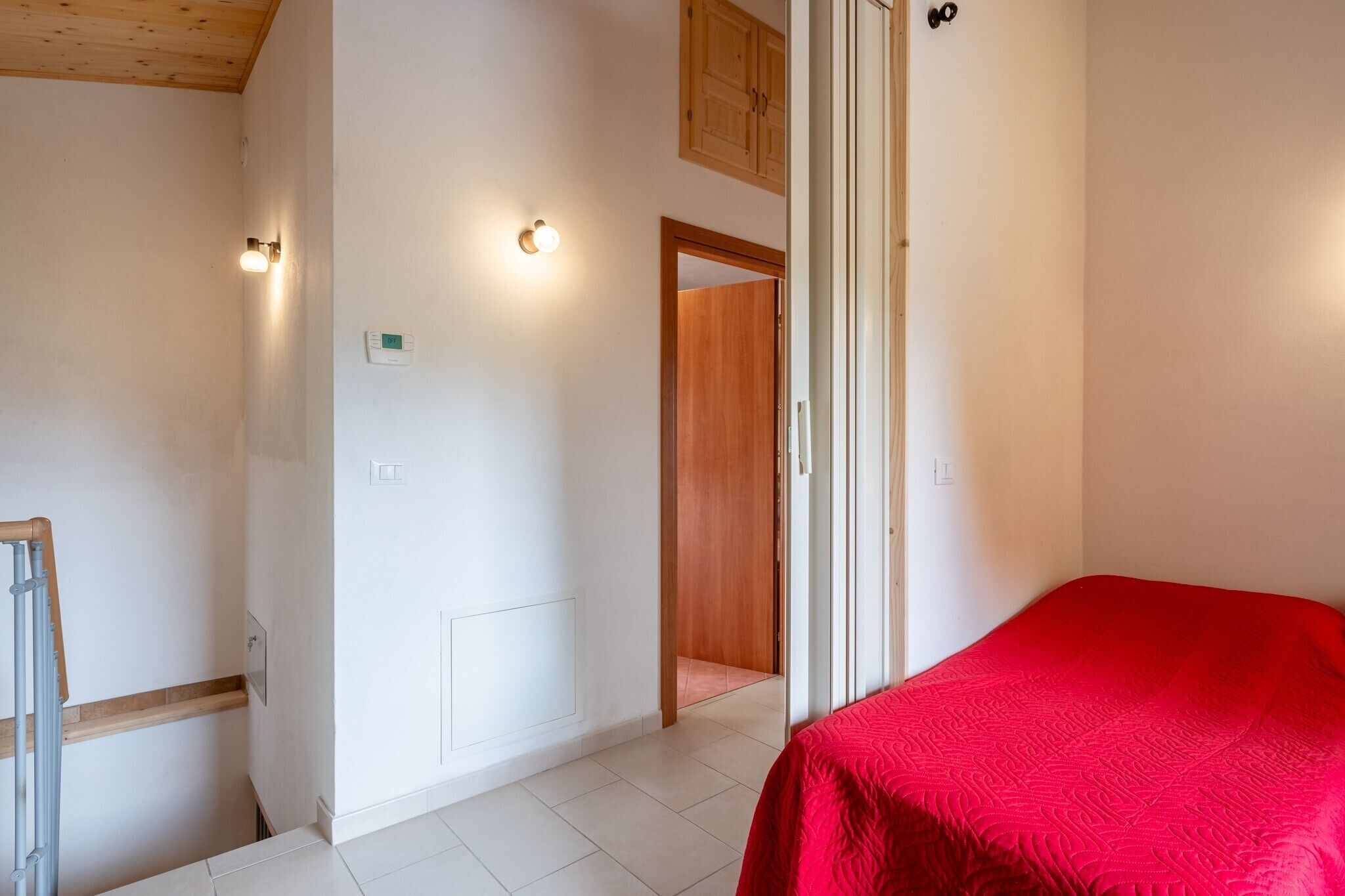 Um quarto com uma cama, uma porta de madeira e um interruptor de luz na parede.