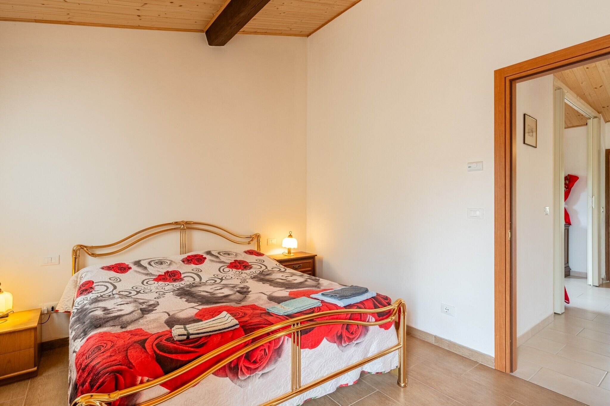 Ein Schlafzimmer mit Bett, Nachttisch, Lampe und einer Tür zu einem anderen Raum.