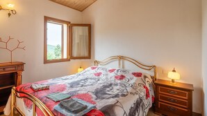 A bedroom with a bed, a nightstand, a dresser, a window, and a wall-mounted lamp.