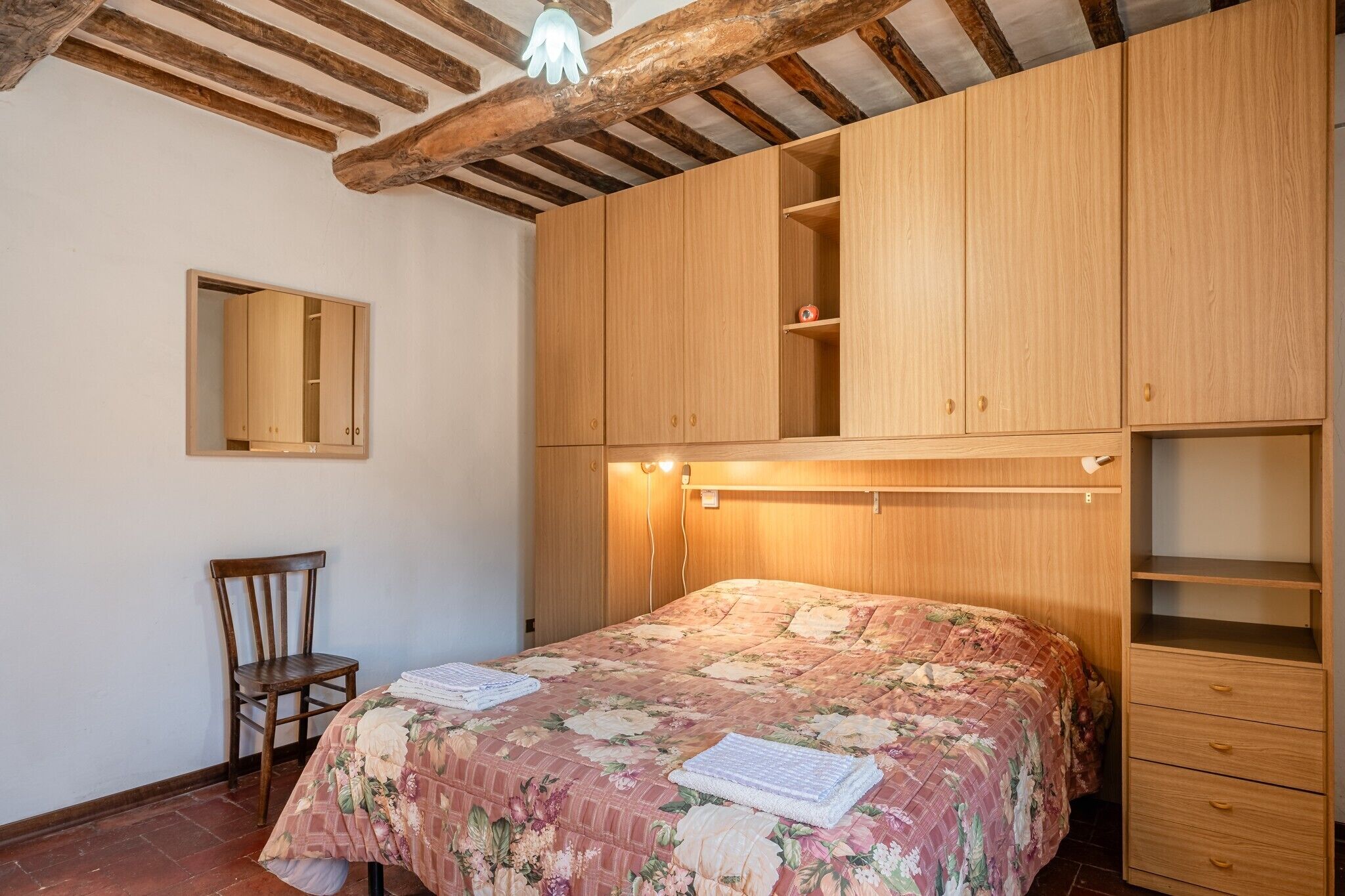A bedroom with a wooden bed, a chair, a mirror, and built-in wooden cabinets.