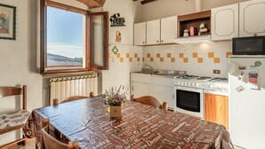 Een keuken met een groot raam, een fornuis, kasten en een eettafel met tafelkleed.