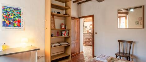 Une pièce avec une bibliothèque en bois, un bureau avec une lampe, un lit recouvert d’une couvre-lit à motifs floraux et un miroir au mur.