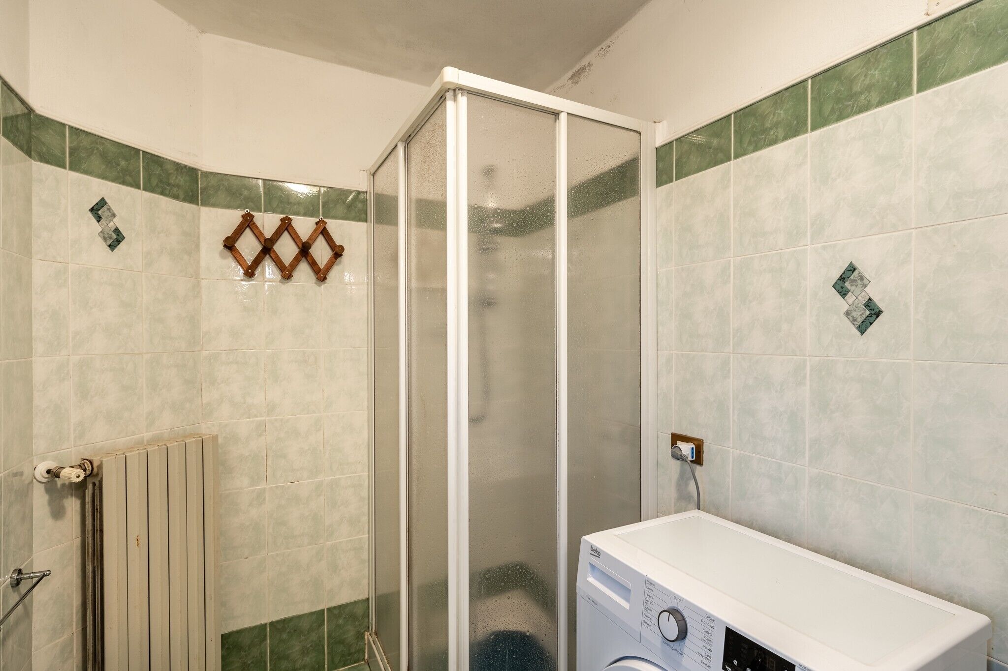 Een badkamer met een douchecabine, een radiator en een wasmachine.
