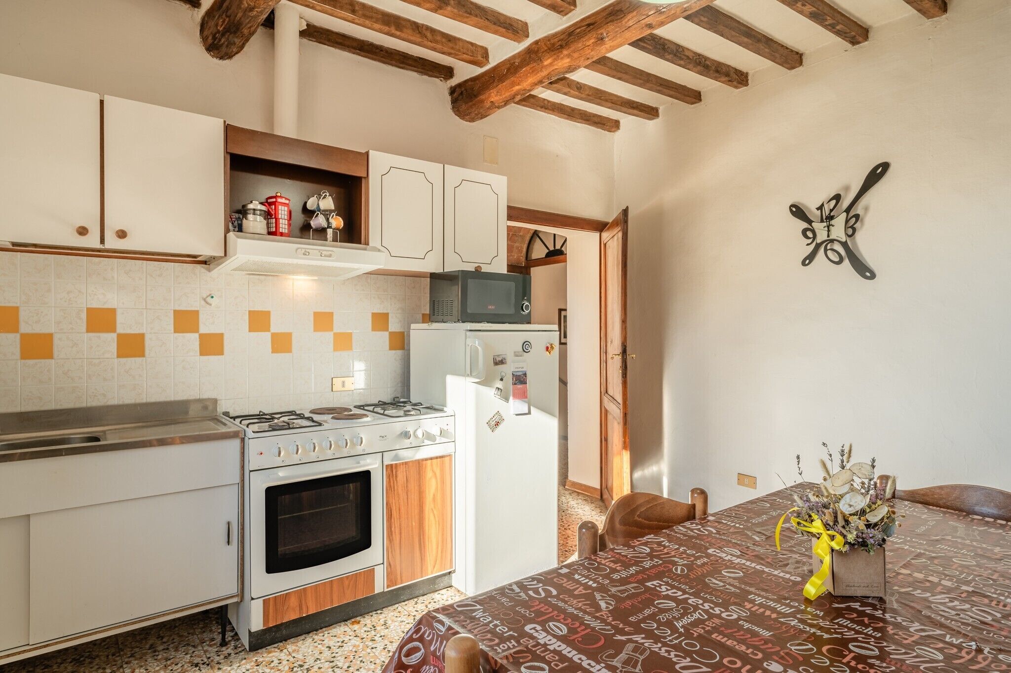 A kitchen with a stove, oven, microwave, and refrigerator. There is a dining table with a yellow ribbon and a bouquet of flowers.