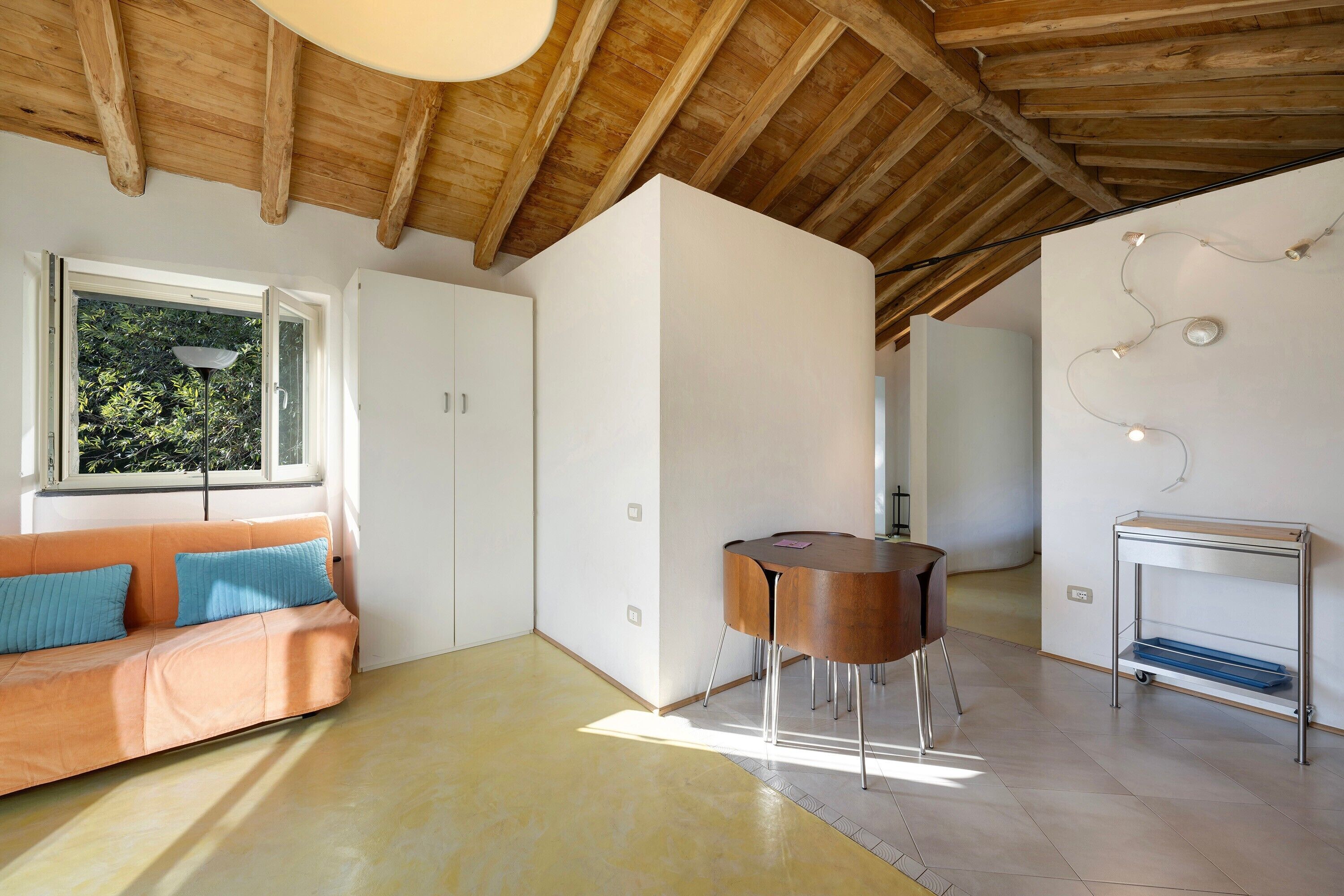 Een modern interieur met een houten plafond, een bank met kussens, een ronde tafel en een klein kastje.