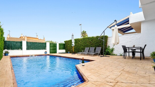 A swimming pool with a tiled edge, a patio area with a table and chairs, and a hedge in the background. - Holiday Home 'Carpa' with Mountain View, Wi-Fi and Air Conditioning (Riumar)
