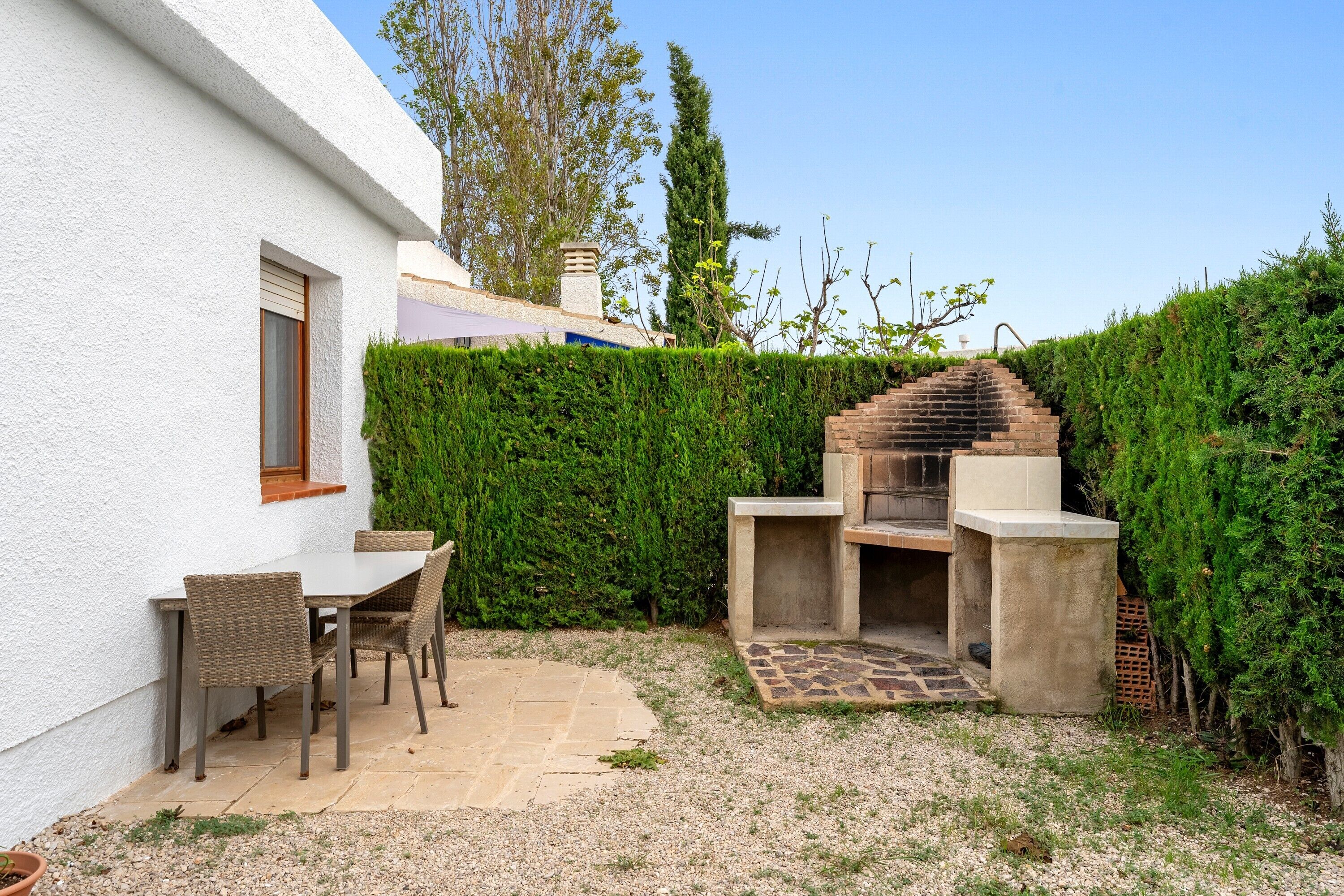 A patio with a table and chairs, a brick barbecue, and a white building with a window.