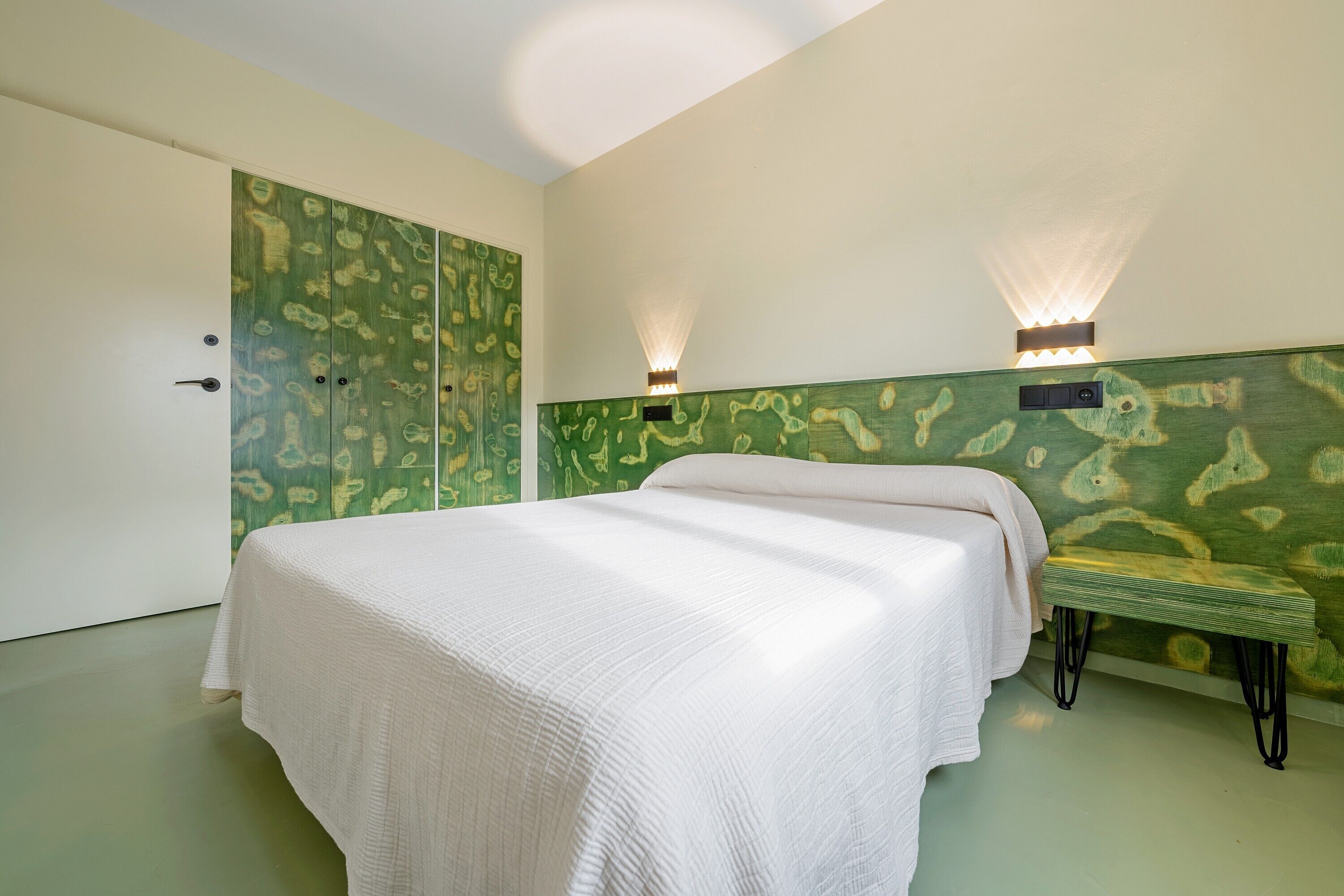 Een slaapkamer met een bed, een bankje, een kledingkast en wandlampen.