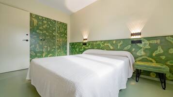 Een slaapkamer met een bed, een bankje, een kledingkast en wandlampen.