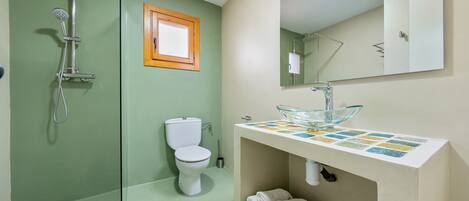 A bathroom with a glass shower, a toilet, a sink with a glass basin, and a mirror above the sink.