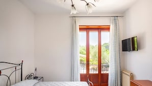 A bedroom with a bed, a nightstand, a TV, a radiator, and a balcony with curtains. - Villa 'Lucia' with Shared Terrace and Wi-Fi (Minturno)