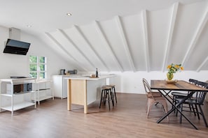Une cuisine moderne dotée d’un îlot central, de meubles blancs et d’un coin repas avec une table et des chaises en bois.