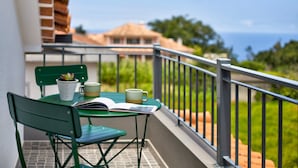 A balcony with a green chair, a small table, a potted plant, and a book.