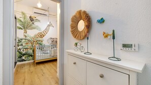 Ein Zimmer mit einem Reisebett, einem Wandspiegel, einem Thermostat und einer Wanddekoration.