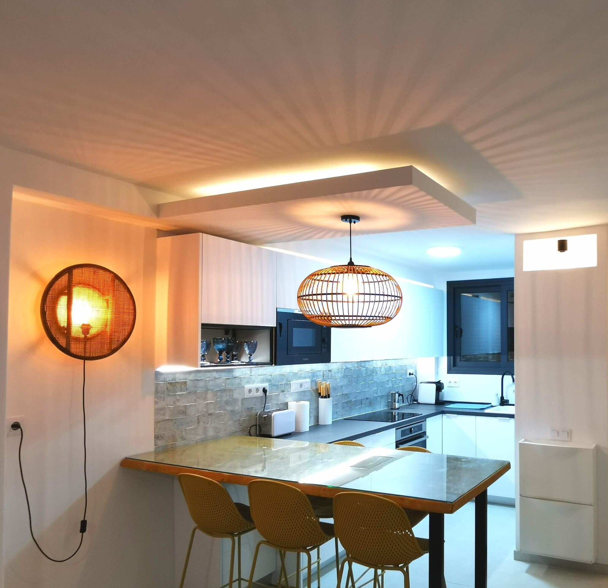 Une cuisine moderne dotée d’un îlot central, de luminaires suspendus et d’un coin repas avec des chaises.