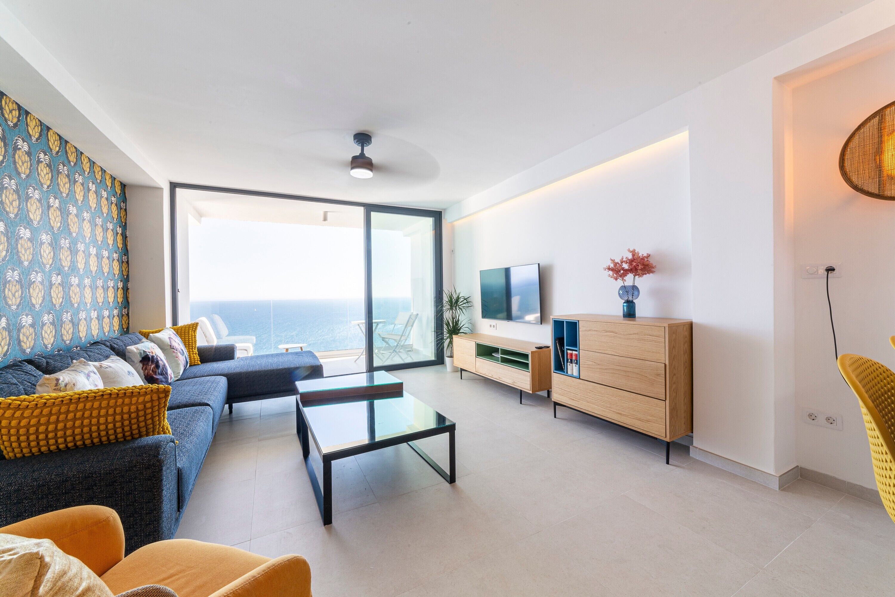Un salon moderne avec un canapé, une table basse, un téléviseur et une vue sur la mer.