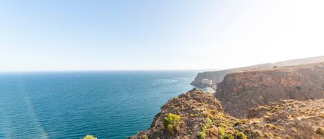 A coastal landscape with a cliff overlooking the sea, a clear sky, and distant buildings.