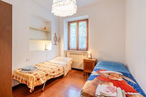 Une petite chambre avec deux lits, une fenêtre, un radiateur et une étagère sur laquelle sont posés divers objets.