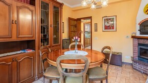 Een eetkamer met een houten tafel, stoelen, een kroonluchter, een open haard en een boekenkast.