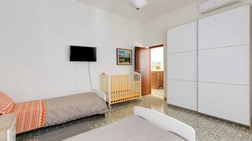 Un dormitorio con cama, cuna, armario, televisor y puerta que da a un balcón.