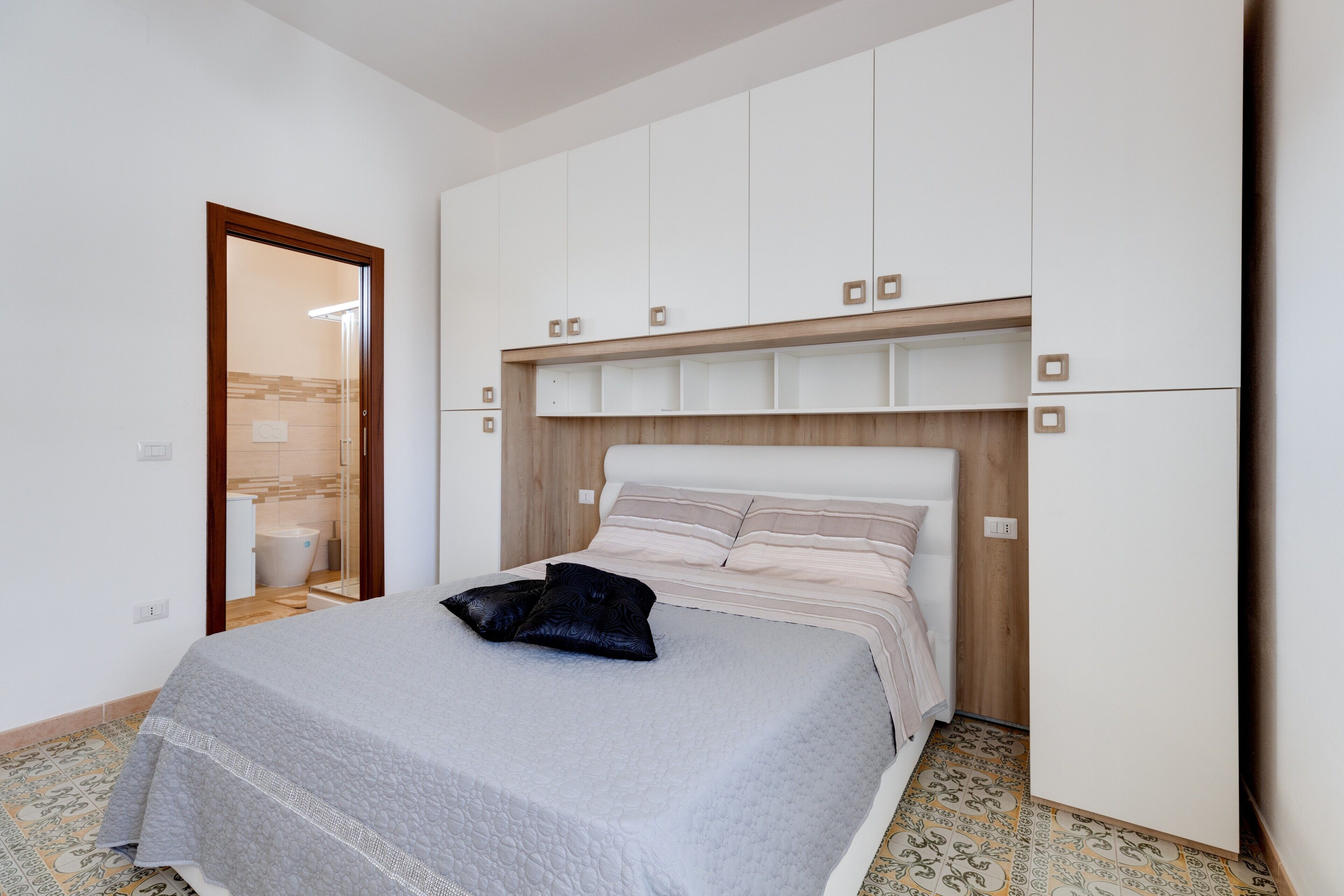 Una camera da letto con un letto, una testiera in legno, un armadio e un bagno visibile attraverso una porta.