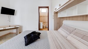 A bedroom with a bed, a desk, a television, and a bathroom visible through an open door. - Holiday Home 'Da Flavia' with Private Terrace, Private Garden and Air Conditioning (riola sardo)