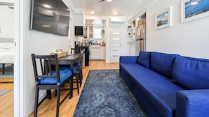 A modern living room with a blue sofa, wooden dining table, and chairs. - Hot Tub/1mi to Downtown/3mi to Coronado/KING Bed/Wifi 300mb+/BBQgrill/Harborside (San Diego)