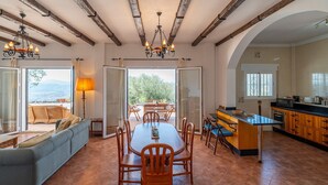 A spacious dining area with a large table and chairs, a sofa, and a kitchen with wooden cabinets. - Villa 'Casa Hyam' with Lake View, Private Pool and Air Conditioning (Alcaucin)