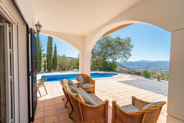 A covered outdoor area with a pool, wicker furniture, and a view of the landscape.