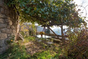 A stone wall, a glass table with metal chairs, and a wooden pergola with climbing plants. - Vacation Home "Gîte De Chapelèche Châtaigniers 7 P" with Private Terrace & Wi-Fi (Gluiras)