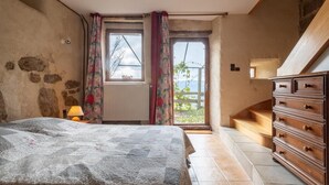 Ein Schlafzimmer mit Bett, Schminktisch, Heizkörper, Fenster mit Vorhängen und Blick ins Freie.