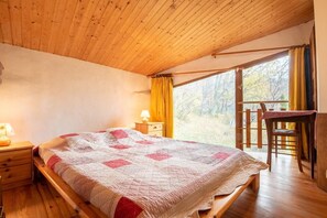 Une chambre confortable avec un lit en bois, une table de chevet, une chaise et une fenêtre avec des rideaux.