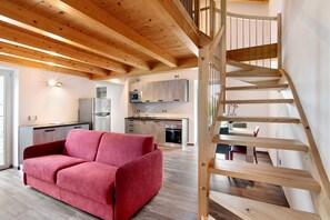 Un intérieur moderne avec un escalier en bois, une cuisine équipée d’appareils électroménagers intégrés et un canapé rouge.