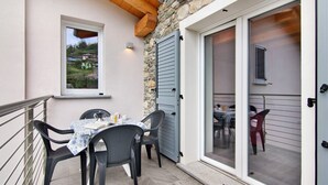 Un área de comedor al aire libre con una mesa y sillas, un muro de piedra y un ventanal corredero que da a otra habitación.