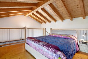 Une chambre avec un plafond en bois, un lit avec une literie à motifs, une table de chevet avec une lampe et un mur blanc.