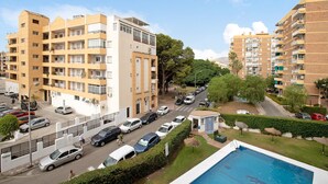 A multi-story residential building with balconies, a swimming pool, and a street with parked cars. - Holiday Apartment "Blue Fish" with Shared Pool, Private Terrace & Wi-Fi (Benalmádena)