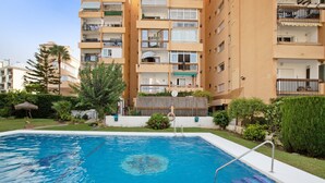 A swimming pool with a metal ladder, surrounded by greenery and a multi-story building with balconies. - Holiday Apartment "Blue Fish" with Shared Pool, Private Terrace & Wi-Fi (Benalmádena)