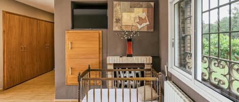 A bedroom with a wooden bed, a wardrobe, a TV, a fireplace, and a window with a view.